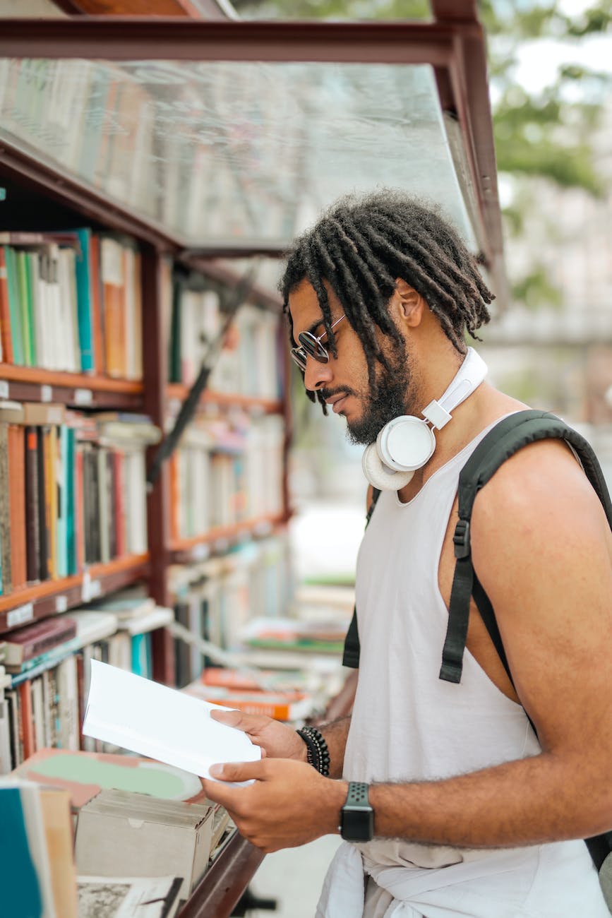 cool trendy ethnic man with dreadlocks reading book on street